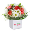 There's a breezy sense of celebration in this bouquet-captured as it stands in a pristine white gift bag, radiating warmth and freshness across New Cross. Layers of coral, peach, and red carnations create a lush tapestry of ruffled petals, their soft edges hinting at gentle fragrance. Bright white daisies, each with a vivid yellow-green eye, break through the arrangement with a dash of joyful energy. Baby's breath floats throughout, its cloudlike blossoms sprinkling delicate innocence over the whole bouquet. On one side, tightly closed, purple-tinged buds quietly introduce depth and anticipation. The whole composition is anchored by a collar of rich, glossy green leaves, their sheen evoking the feeling of a dewy morning in Fordham Park. The image's clean background sharpens every colour and detail, while the sturdy ribbon handles atop the white bag promise easy carrying for same-day delivery throughout New Cross. Expertly crafted to bring smiles for birthdays, thank-yous, or new beginnings, this arrangement springs to life as a testament to the local florists' skill, heartfelt care, and understanding of what makes each moment in New Cross truly special.